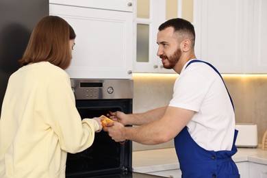 Repairman showing woman how to use multimeter near oven in kitchen