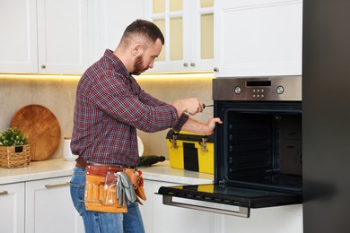 Repairman with screwdriver fixing oven in kitchen