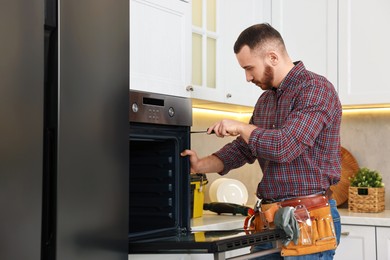 Repairman with screwdriver fixing oven in kitchen