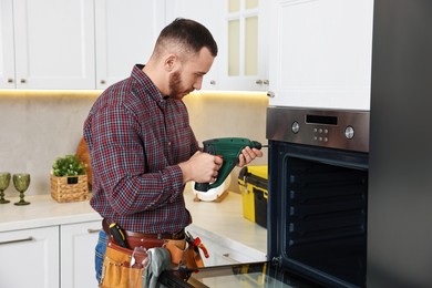 Repairman with electric screwdriver fixing oven in kitchen