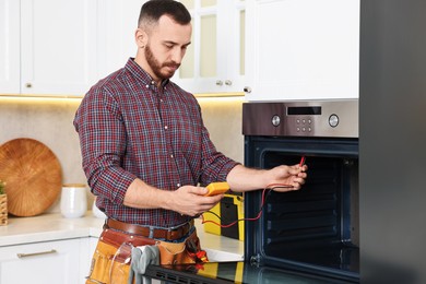 Repairman testing oven element with multimeter in kitchen