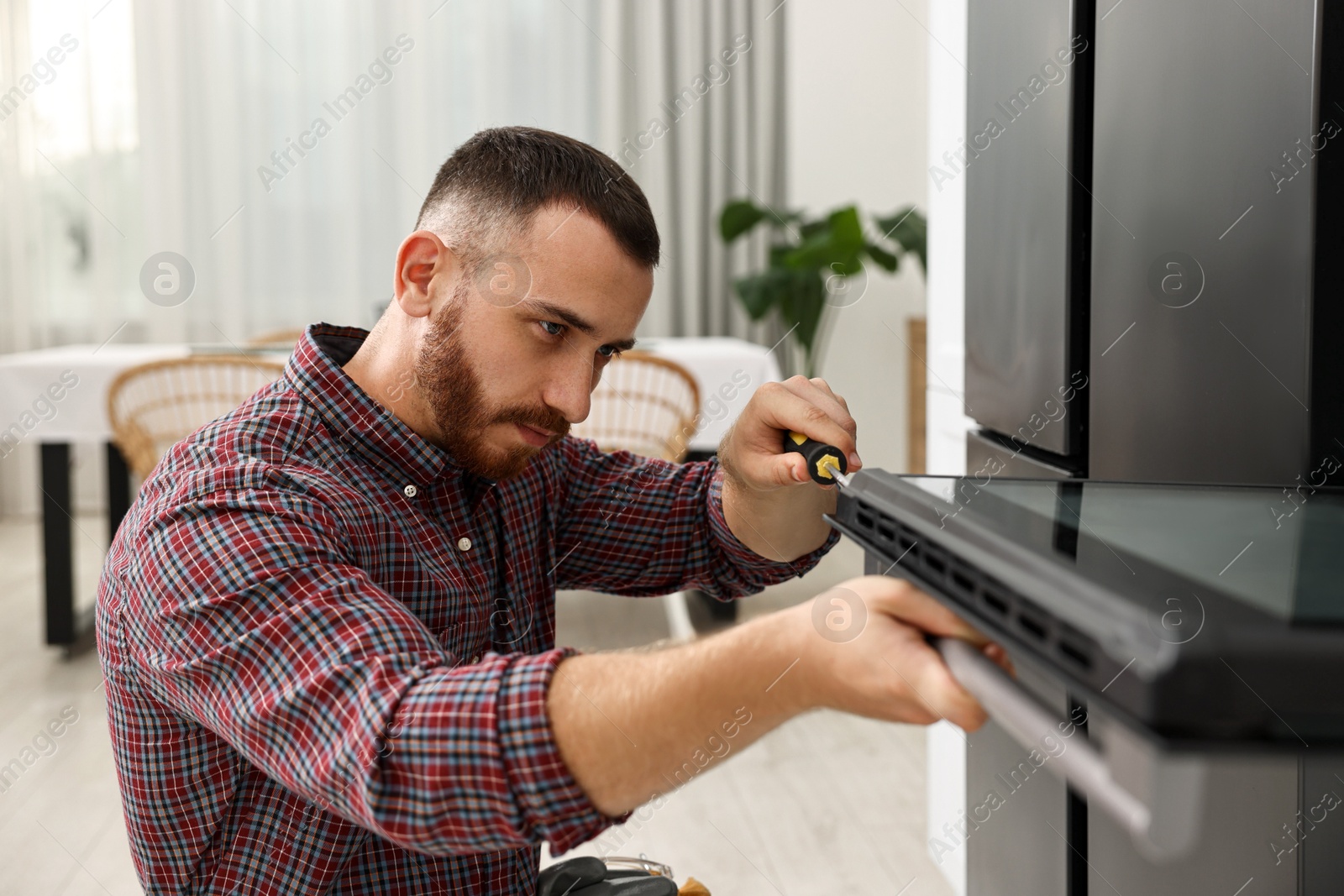 Photo of Repairman with screwdriver fixing oven at home