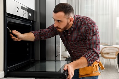 Photo of Repairman with screwdriver fixing oven at home