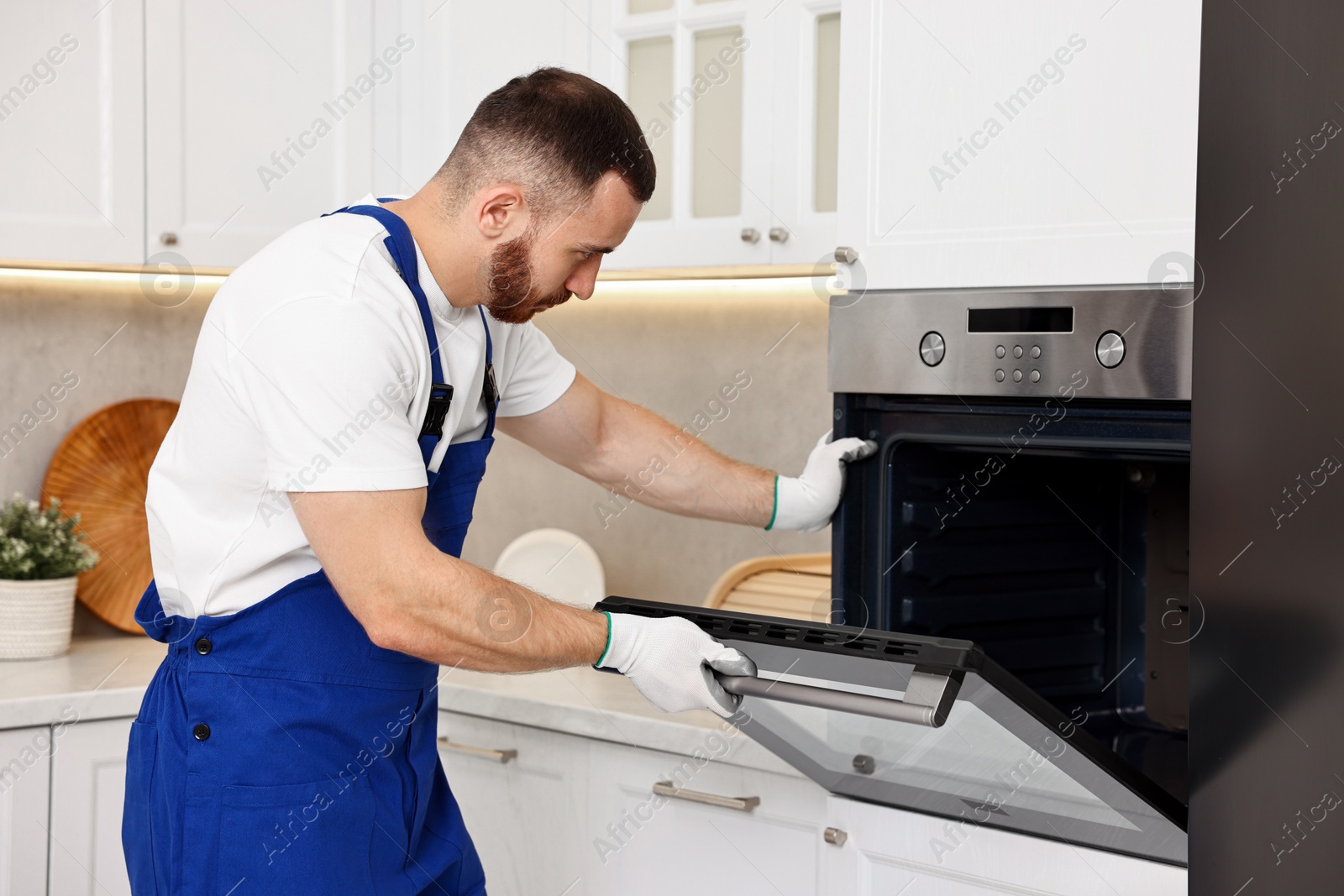 Photo of Repairman in uniform examining oven in kitchen