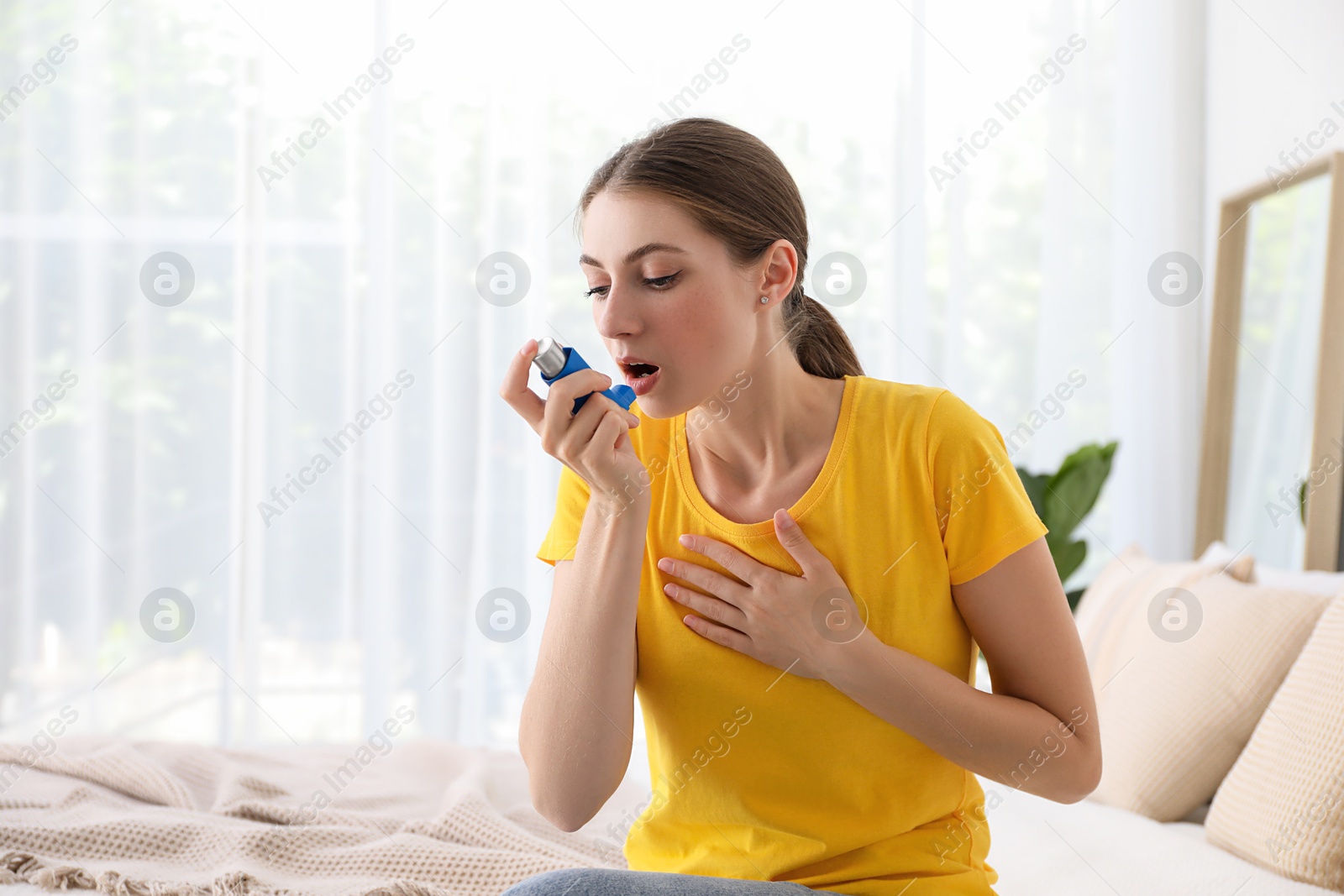 Photo of Young woman using asthma inhaler at home. Space for text