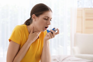 Young woman using asthma inhaler at home. Space for text