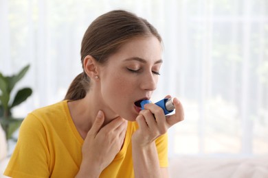 Young woman using asthma inhaler at home. Space for text