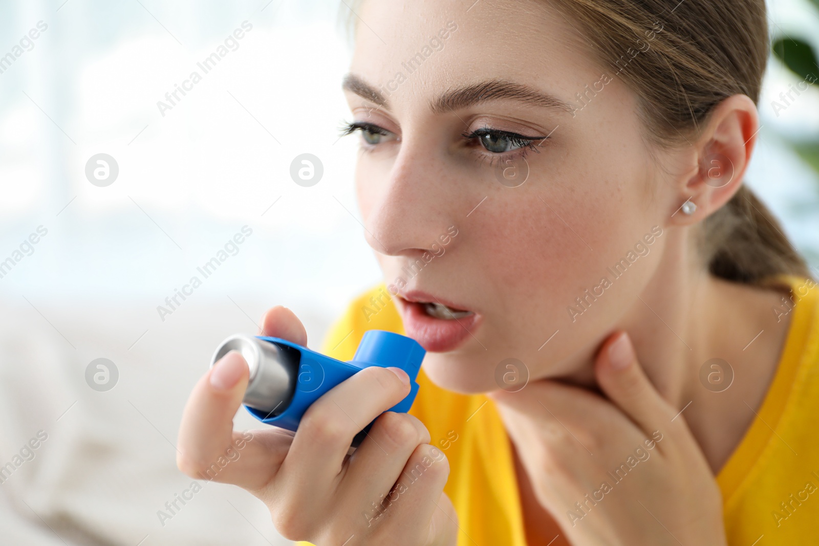 Photo of Young woman using asthma inhaler at home, closeup