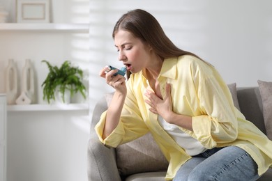 Young woman using asthma inhaler at home. Space for text