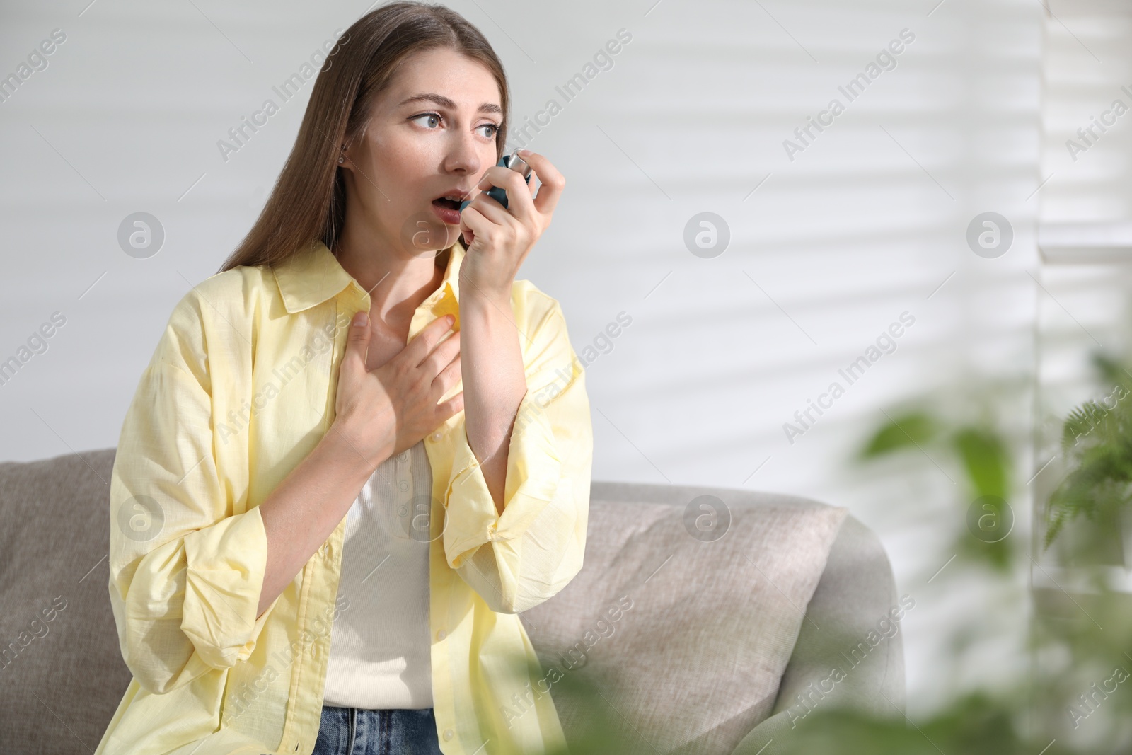 Photo of Young woman using asthma inhaler at home. Space for text