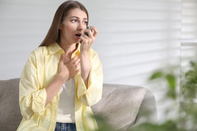 Young woman using asthma inhaler at home. Space for text