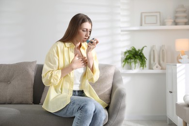 Young woman using asthma inhaler at home. Space for text