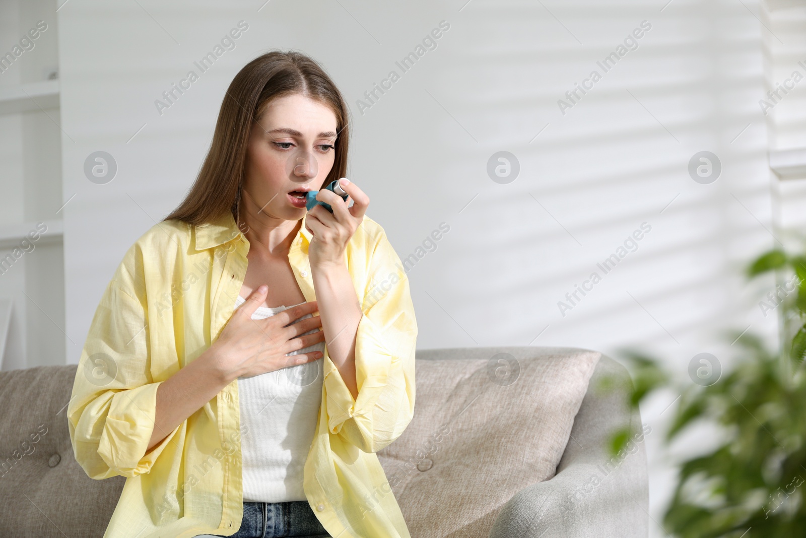 Photo of Young woman using asthma inhaler at home. Space for text