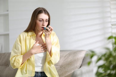 Young woman using asthma inhaler at home. Space for text