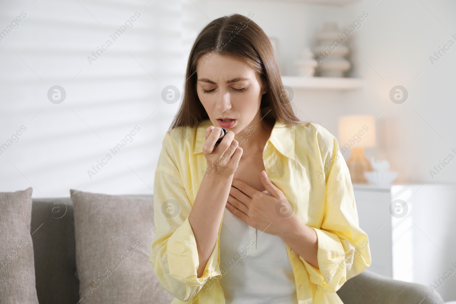 Photo of Young woman using asthma inhaler at home