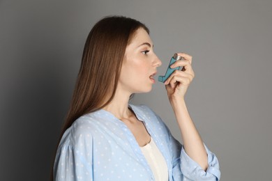 Photo of Young woman using asthma inhaler on grey background