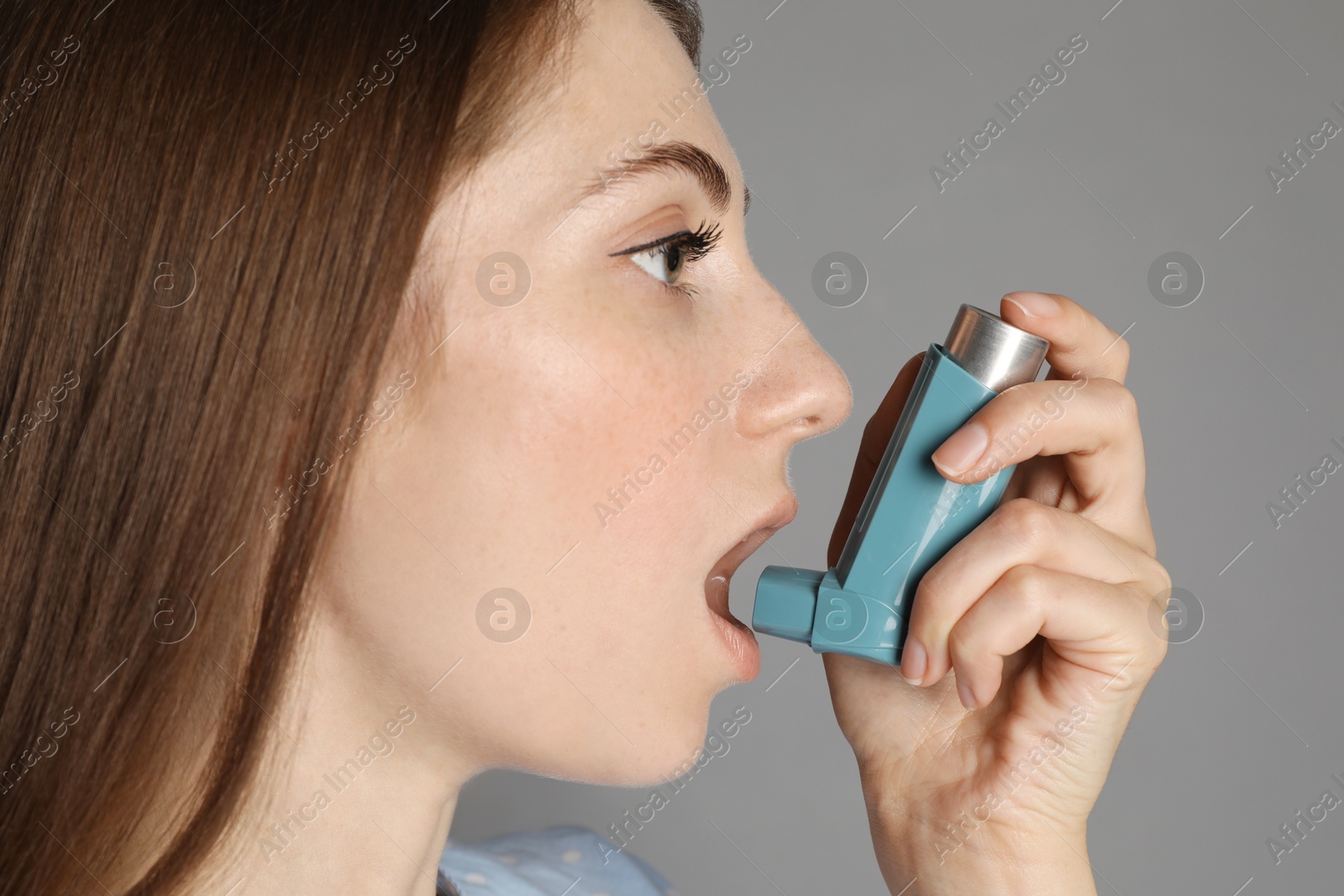 Photo of Young woman using asthma inhaler on grey background, closeup