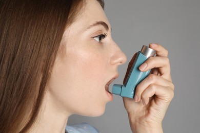 Photo of Young woman using asthma inhaler on grey background, closeup