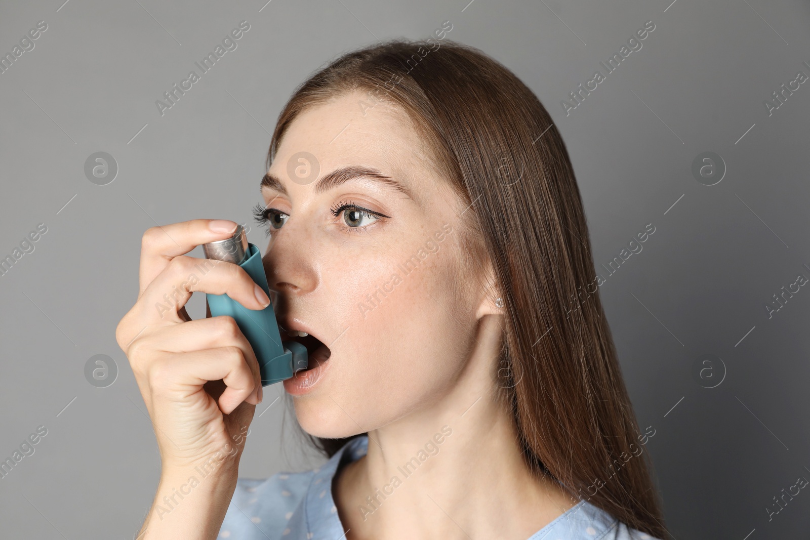 Photo of Young woman using asthma inhaler on grey background