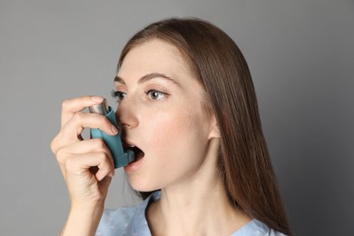 Young woman using asthma inhaler on grey background