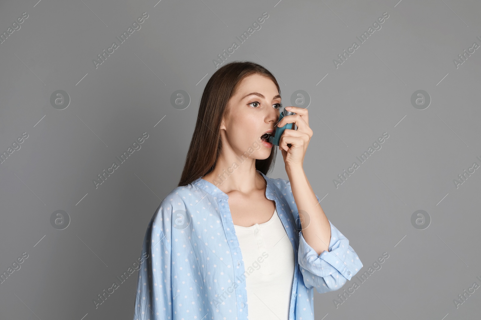 Photo of Young woman using asthma inhaler on grey background