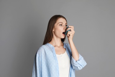 Young woman using asthma inhaler on grey background