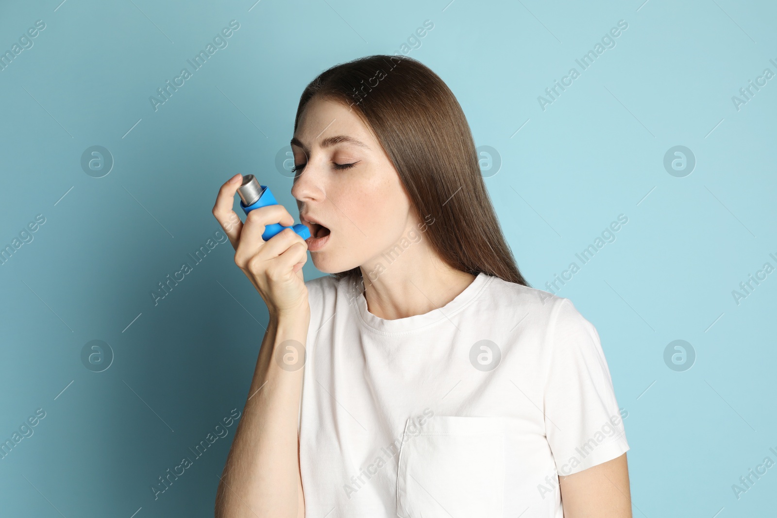 Photo of Young woman using asthma inhaler on light blue background