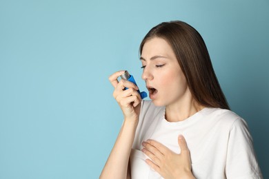 Young woman using asthma inhaler on light blue background. Space for text