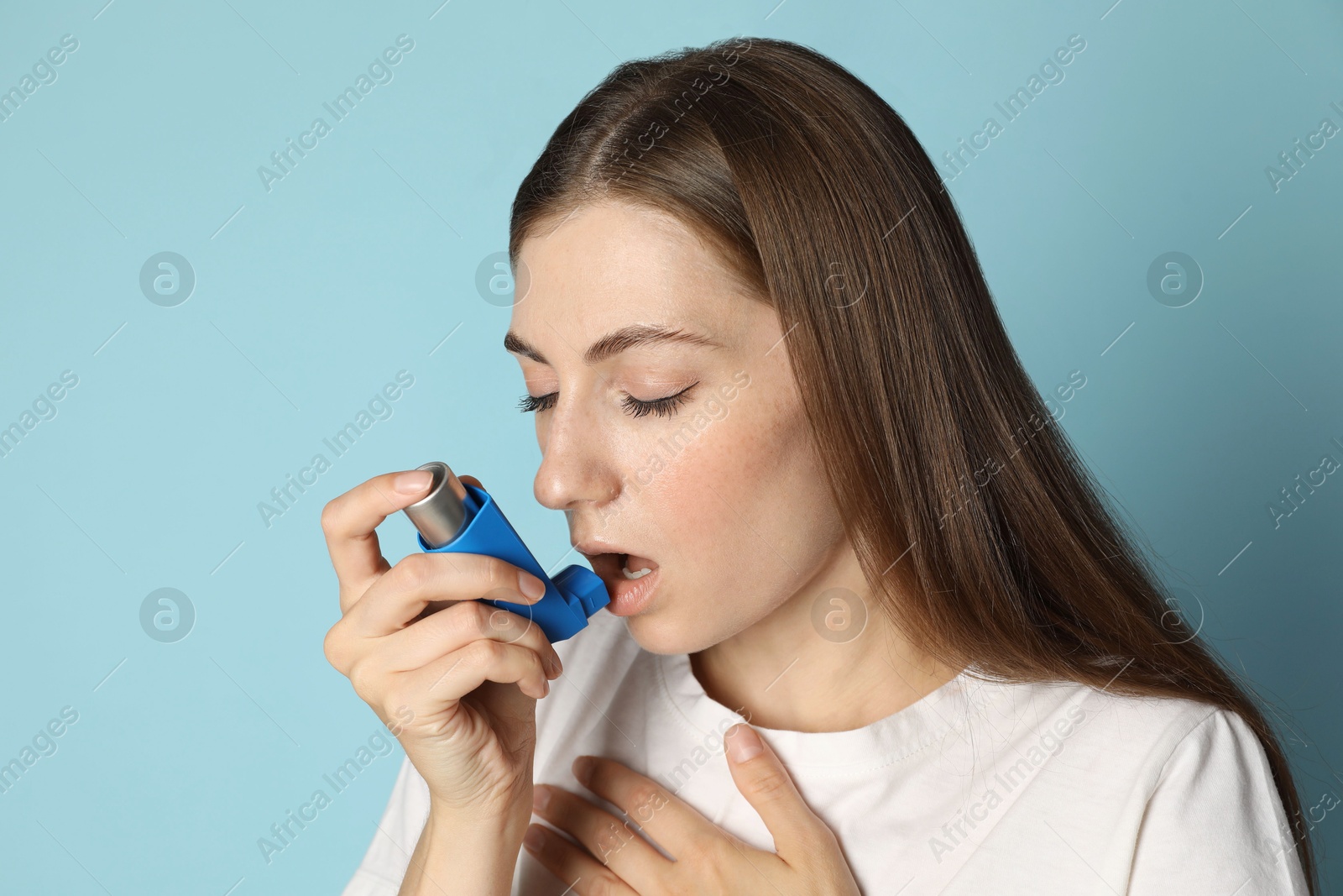 Photo of Young woman using asthma inhaler on light blue background