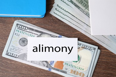 Photo of Alimony. Dollar banknotes, blank card and notebook on wooden table, top view