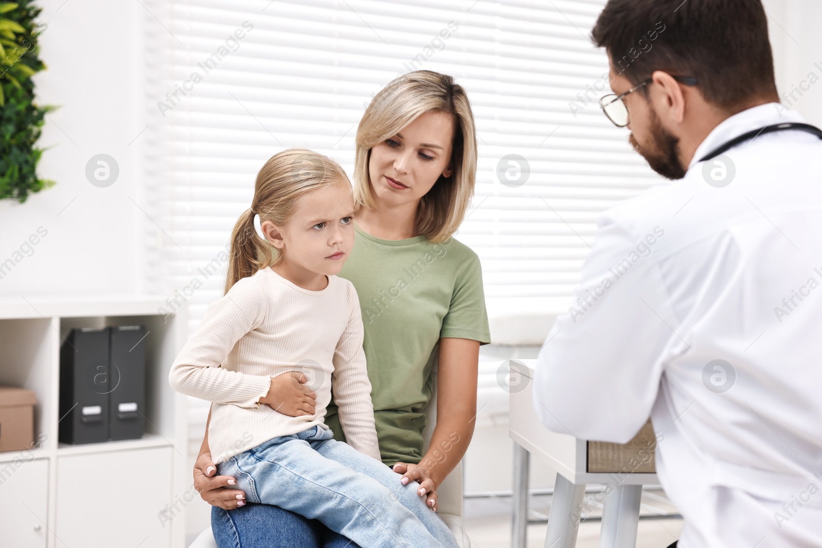 Photo of Doctor consulting little girl with stomach pain and her mother in hospital, back view