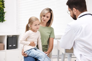 Doctor consulting little girl with stomach pain and her mother in hospital, back view