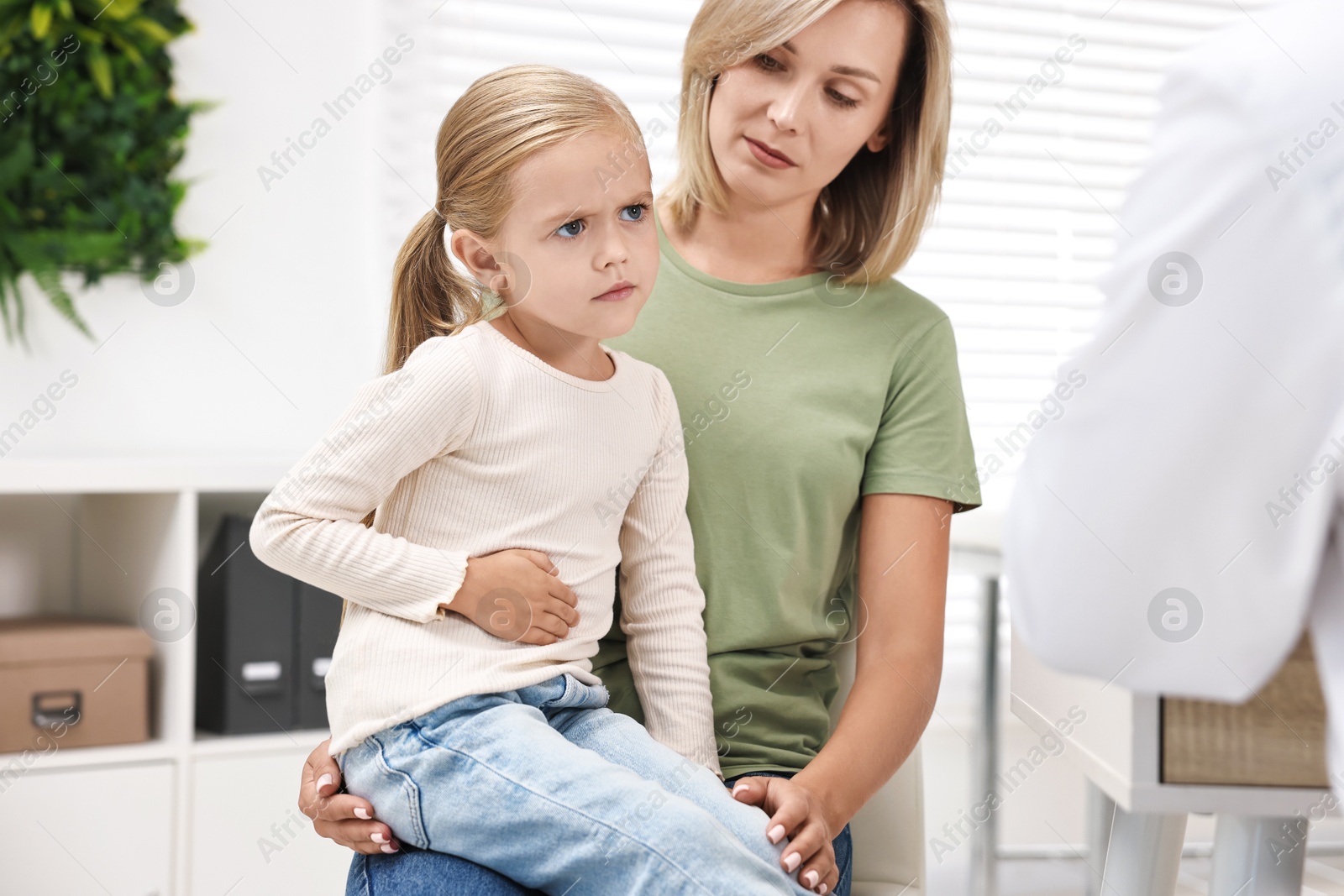 Photo of Little girl with stomach pain and her mother having appointment with doctor in hospital