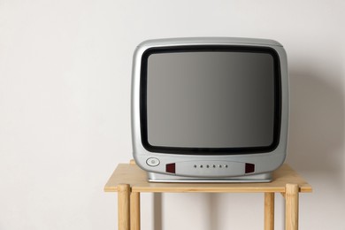 Photo of Retro tv set on wooden shelf against white wall. Space for text