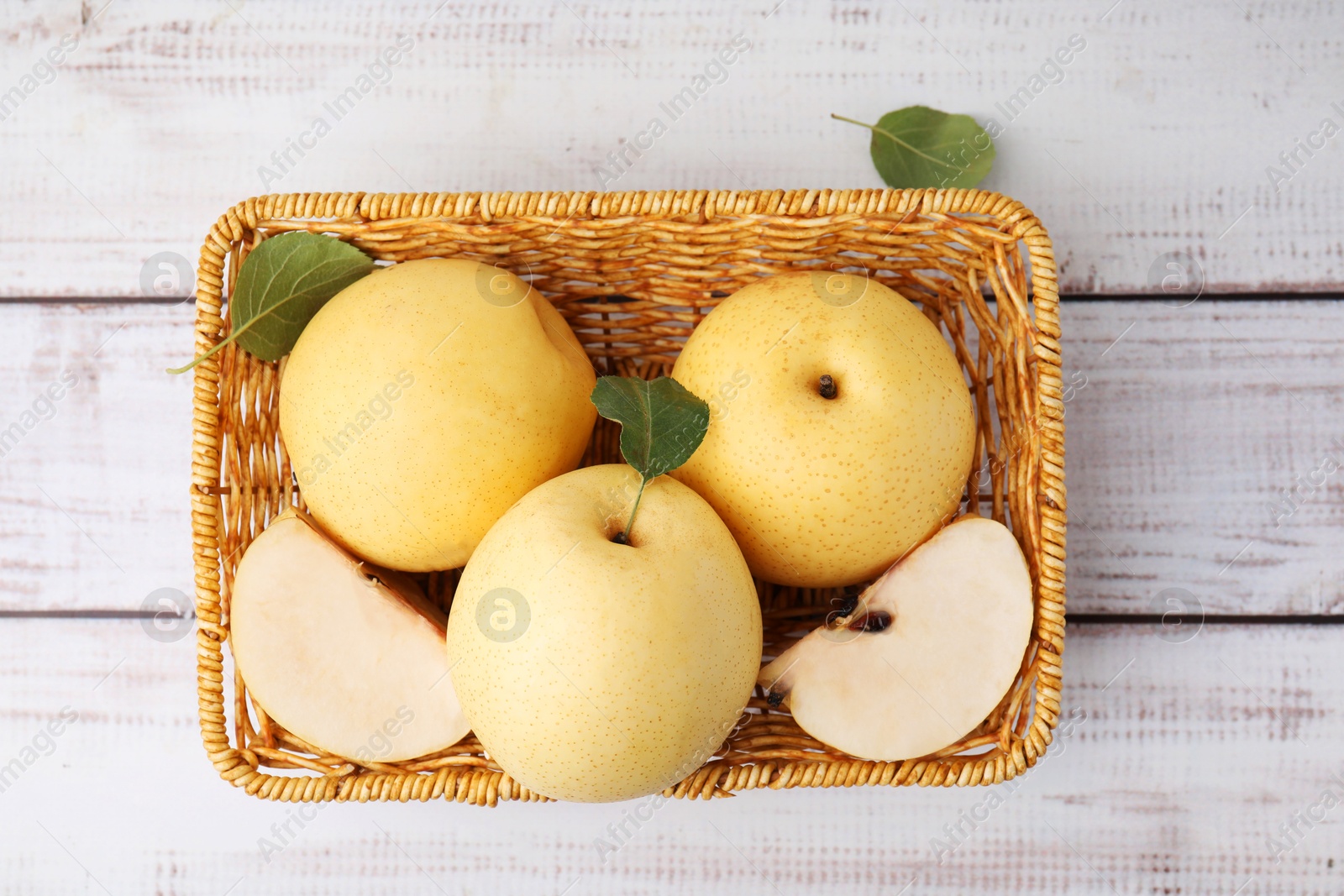 Photo of Delicious fresh apple pears in wicker basket on white wooden table, top view