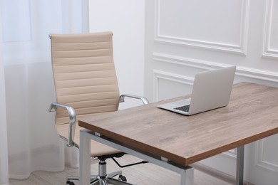 Beige leather chair, laptop and desk in office