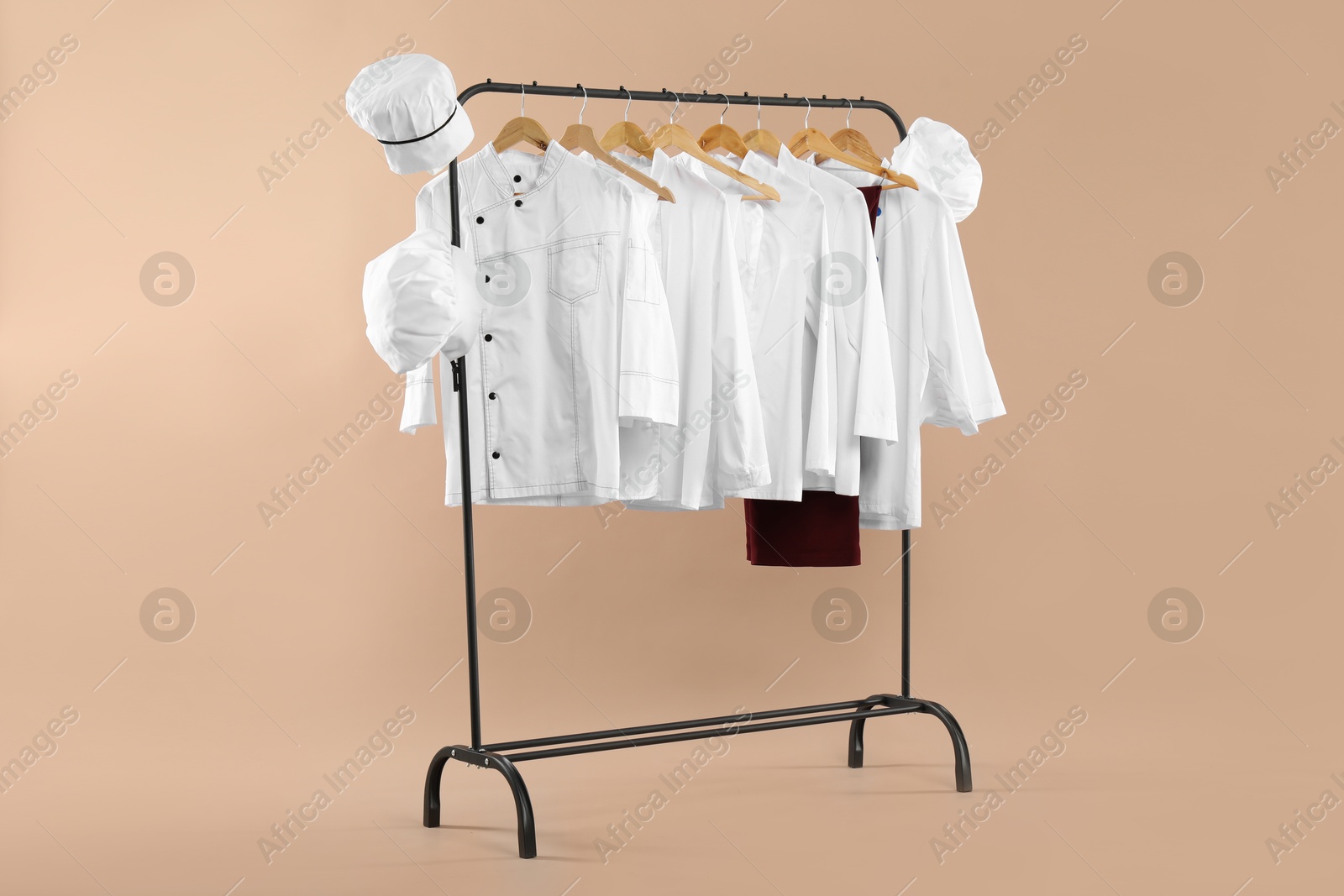 Photo of Different chef's uniforms on clothing rack against beige background, space for text