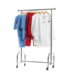 Photo of Different medical workers' uniforms and stethoscope on clothing rack against white background