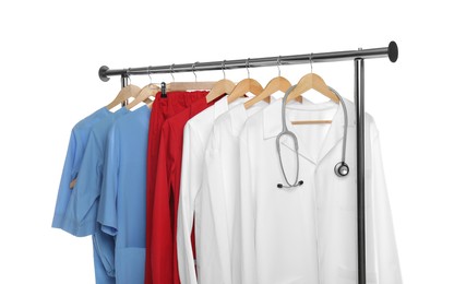 Different medical workers' uniforms and stethoscope on clothing rack against white background