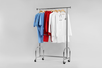 Photo of Different medical workers' uniforms and stethoscope on clothing rack against white background