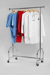 Photo of Different medical workers' uniforms and stethoscope on clothing rack against white background