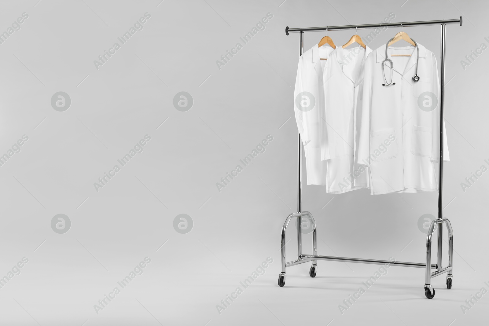 Photo of Doctor's coats with stethoscope on clothing rack against white background