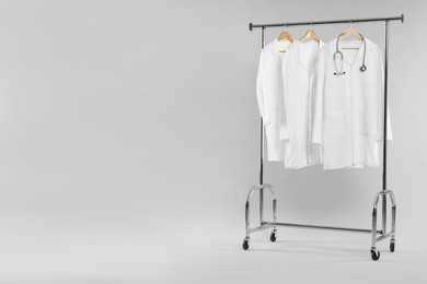 Photo of Doctor's coats with stethoscope on clothing rack against white background