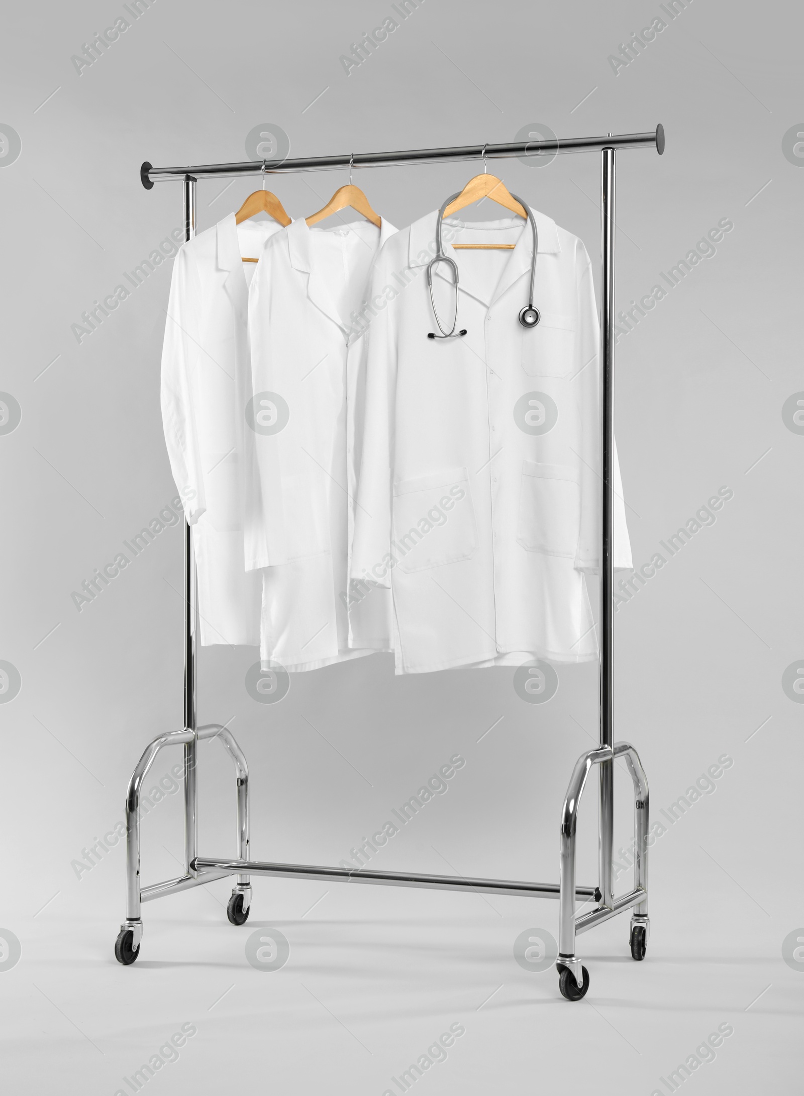 Photo of Doctor's coats with stethoscope on clothing rack against white background