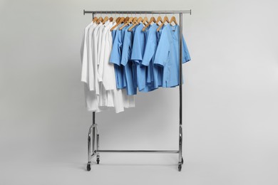 Photo of Different medical workers' uniforms on clothing rack against white background