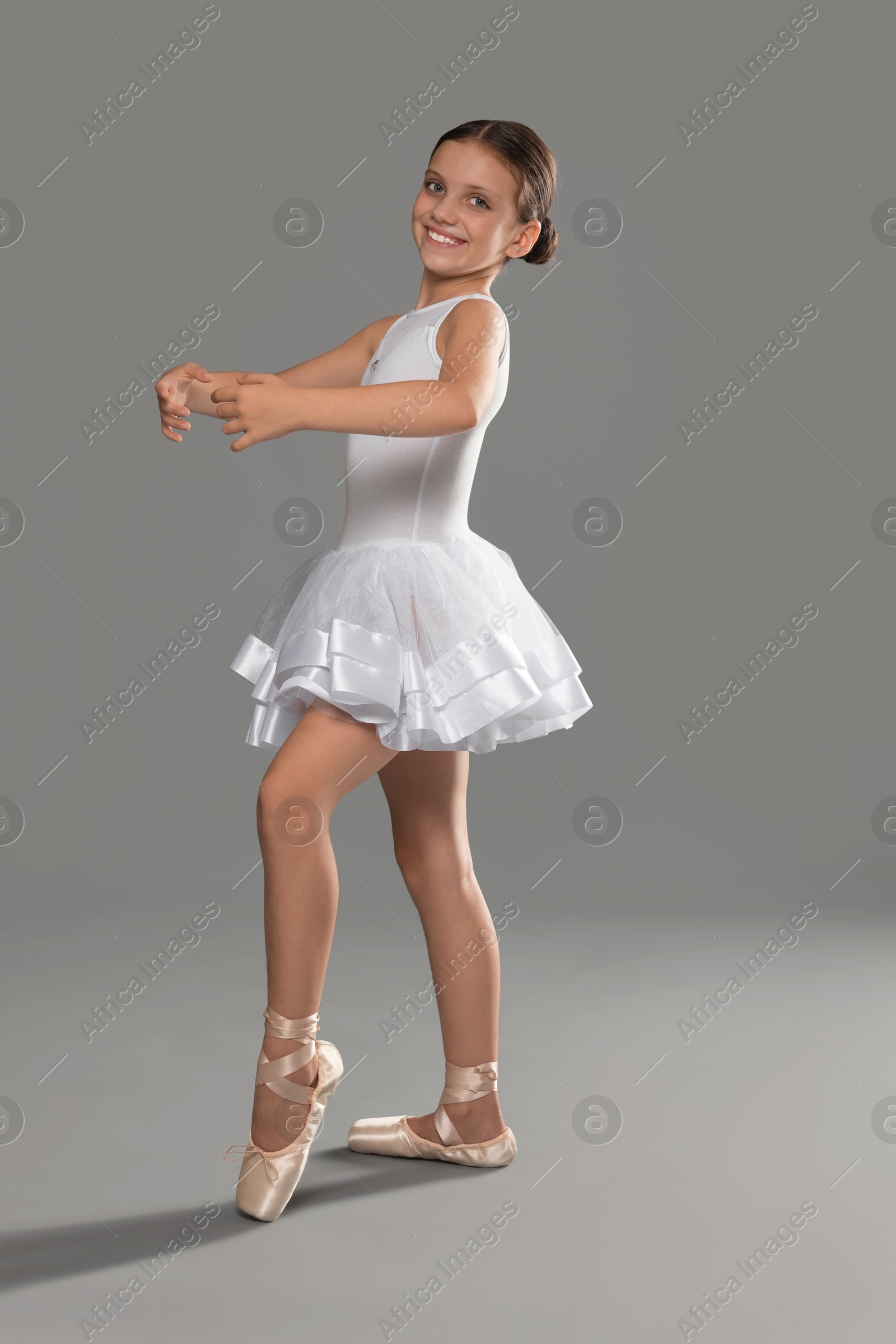 Photo of Cute little ballerina dancing on grey background