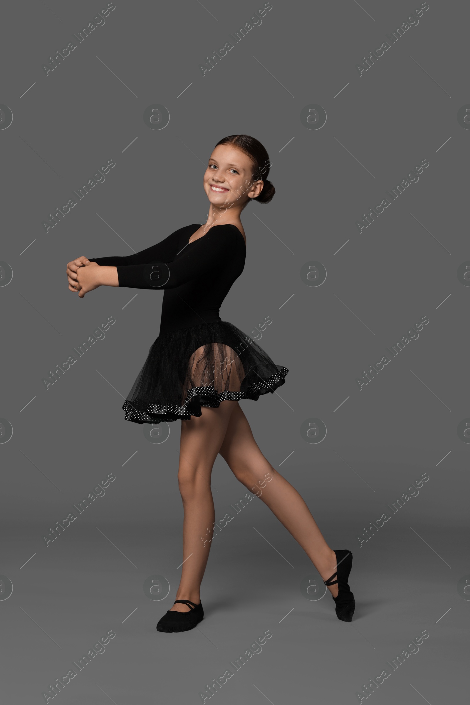 Photo of Little ballerina practicing dance moves on grey background