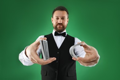 Professional croupier shuffling cards on green background, selective focus