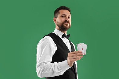 Photo of Professional croupier with playing cards on green background