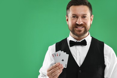 Professional croupier with playing cards on green background, space for text